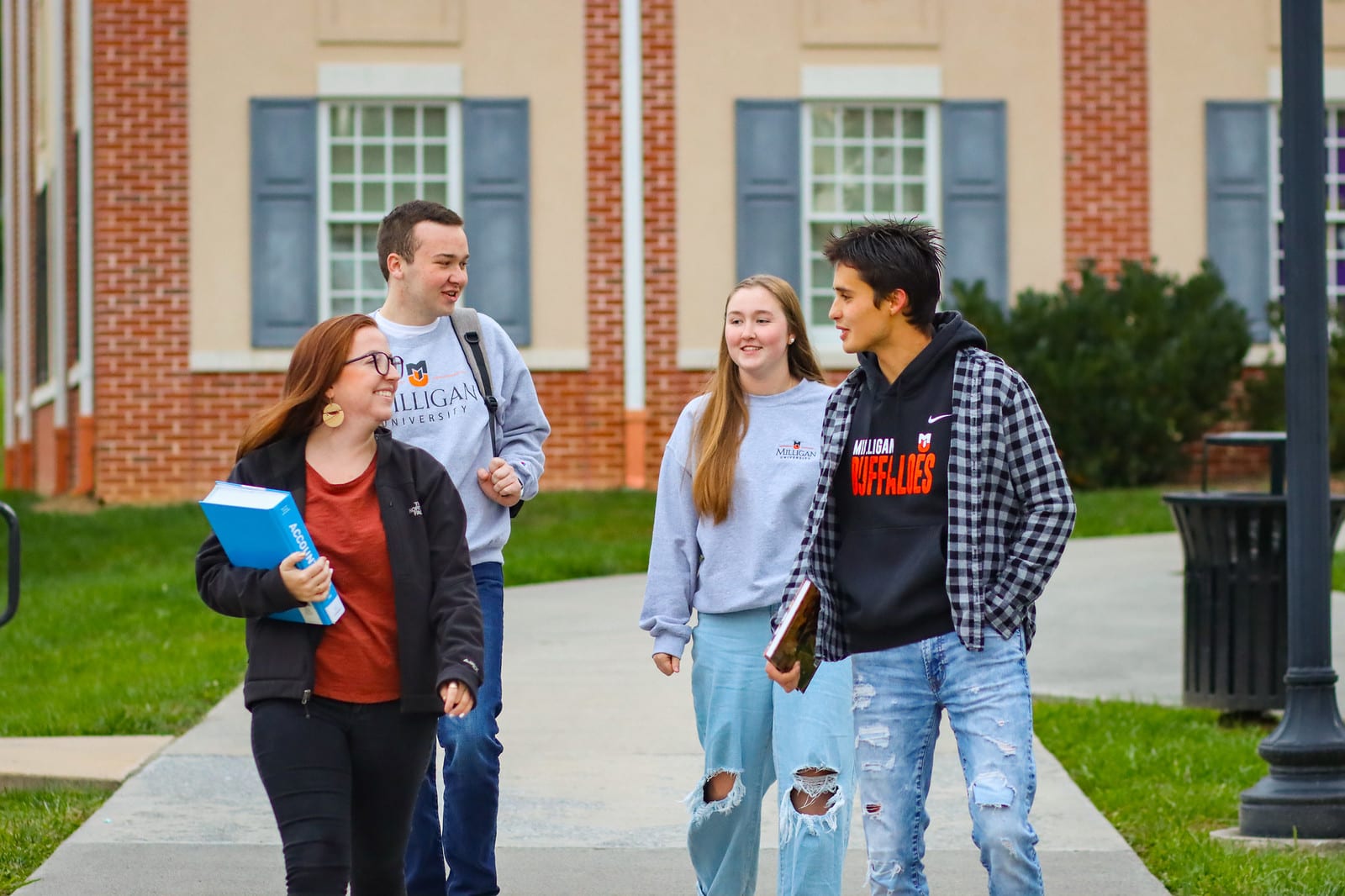 Four students walking on a sidewalk carrying books